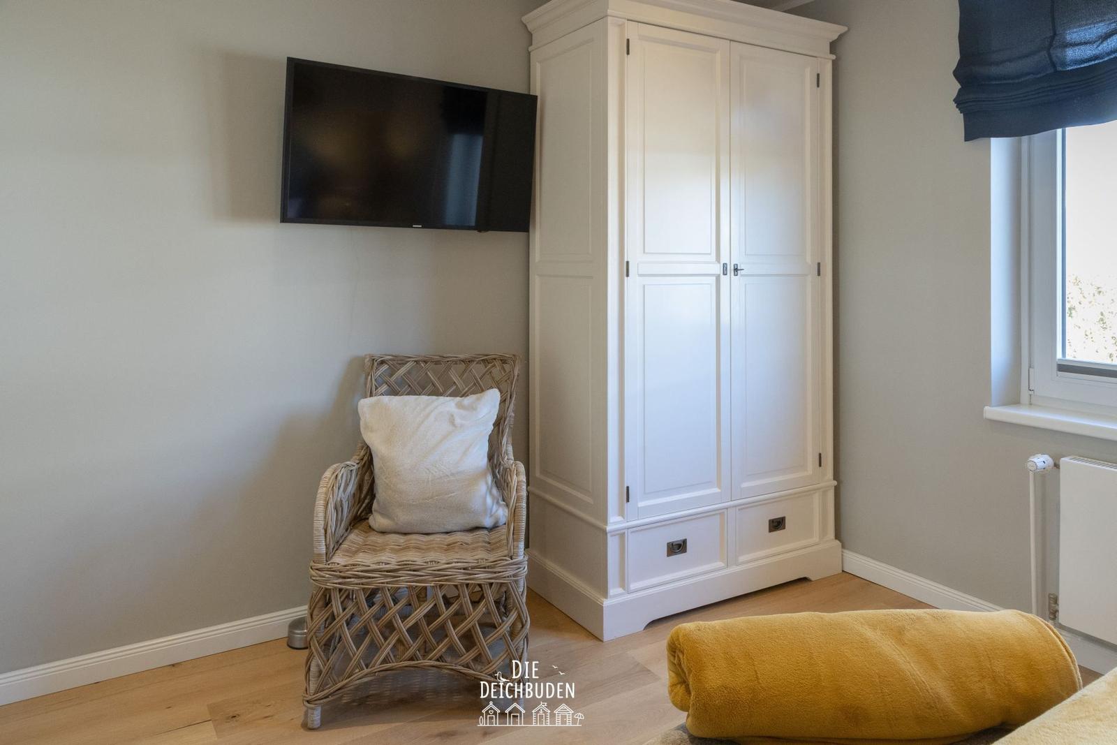 Schlafzimmer mit weißen Schrank, Wickerstuhl und Wandfernseher