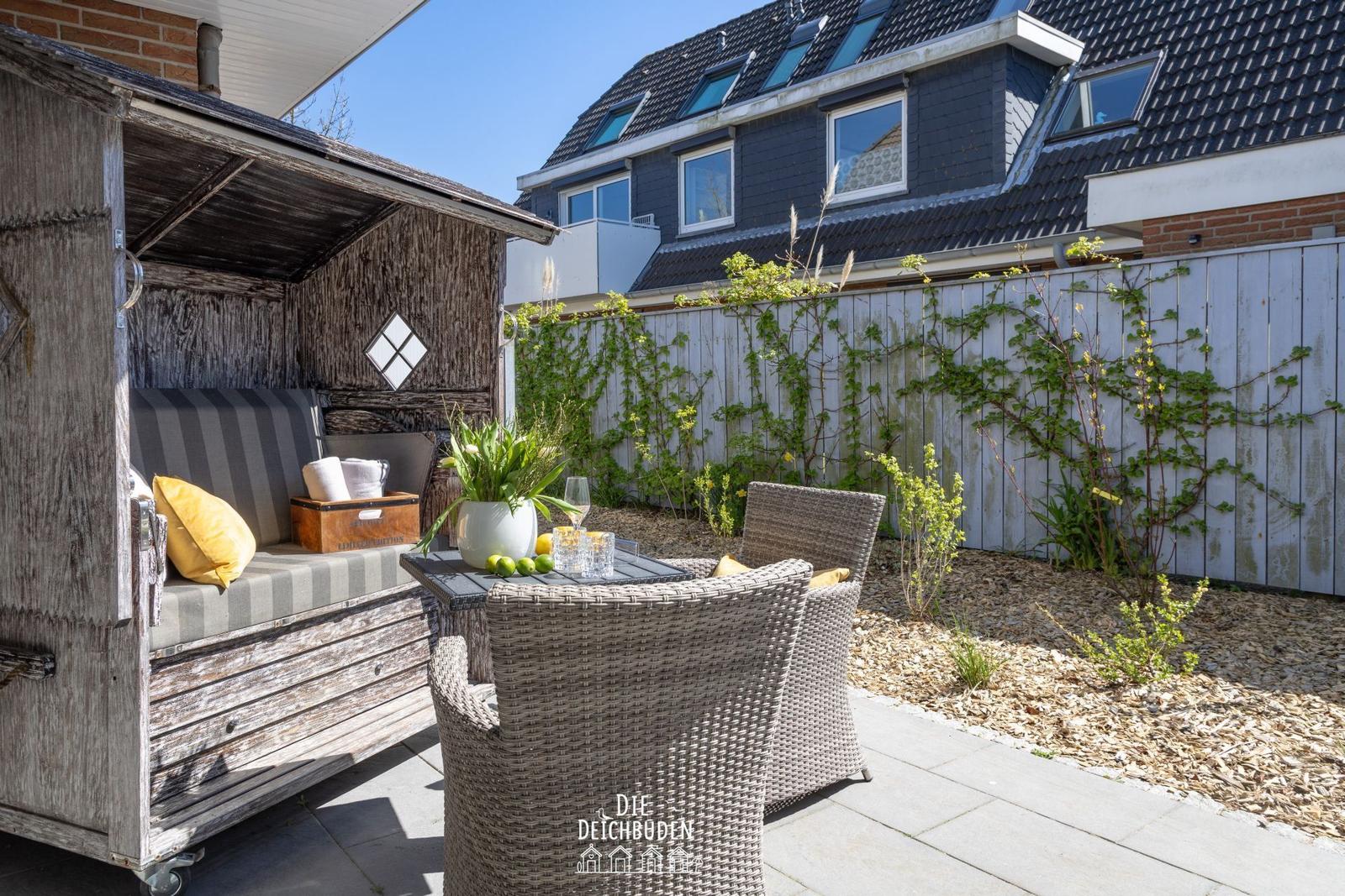 Terrasse mit Holzschuppen, Sitzgelegenheiten und Pflanzen. Hinterhof mit Zaun und Gartengrund.