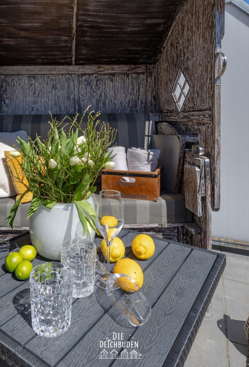 Terrassenbereich mit Holzgestell, Tisch mit Früchten und Blumen, Sitzbank mit Kissen.