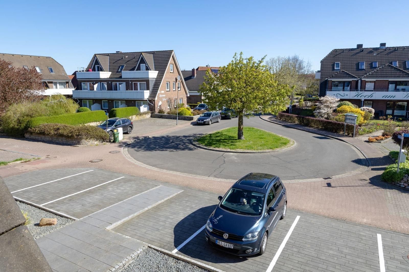 Parkplatz mit Auto vor Wohnhäusern und Grünfläche