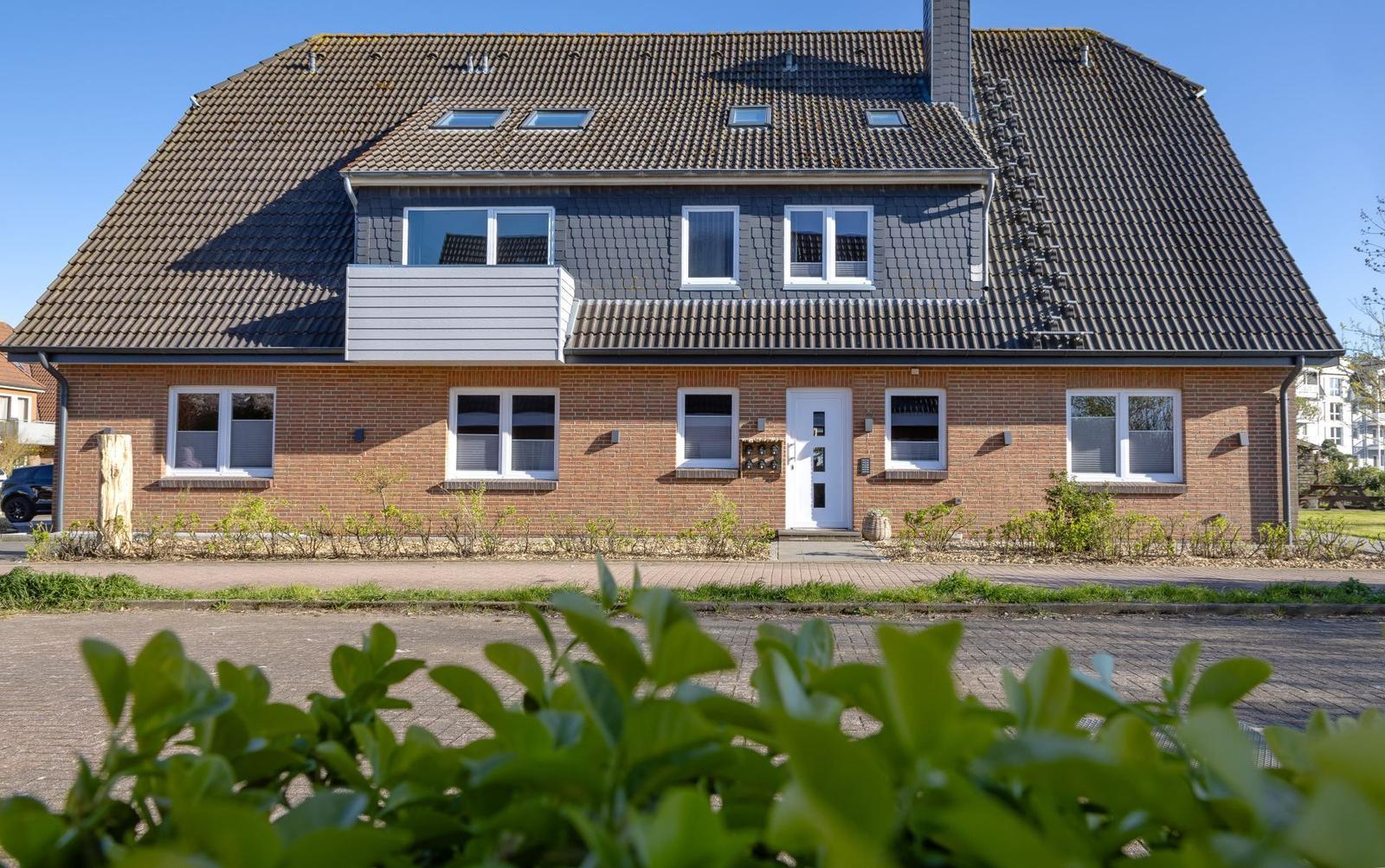 Ein zweistöckiges Haus mit rotem Backstein und dunklem Dach. Weiße Fenster und Tür.