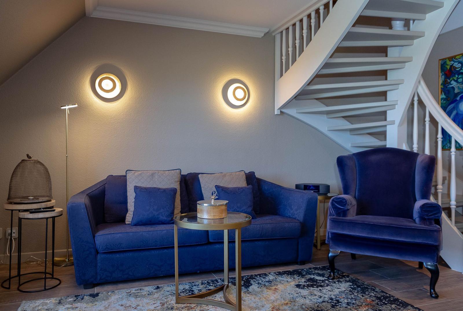 Ein Wohnzimmer mit blauem Sofa, Sessel und einer Treppe.