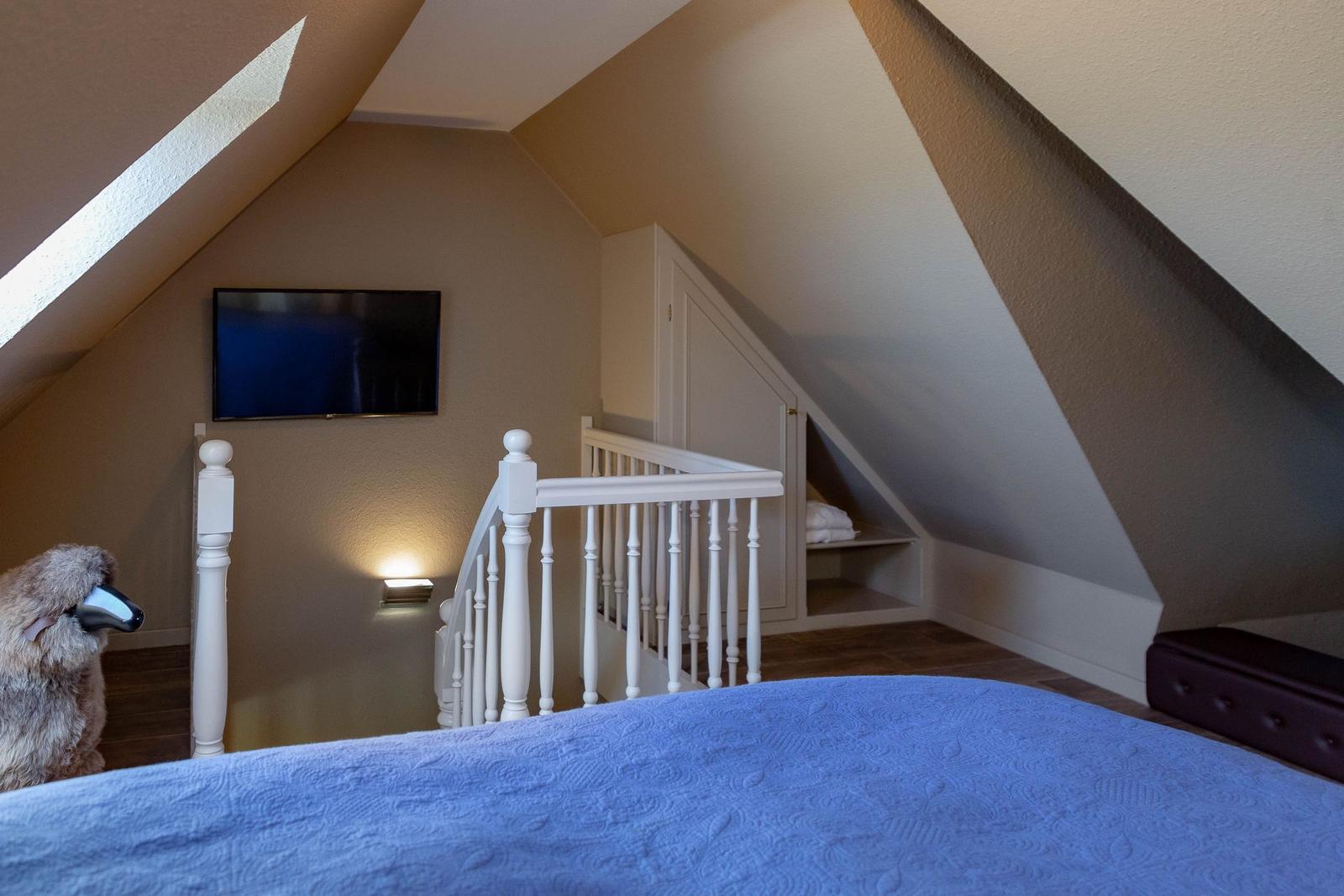 Schlafzimmer mit Dachschrägen, Bett, Fernseher und kleinem Treppenaufgang.