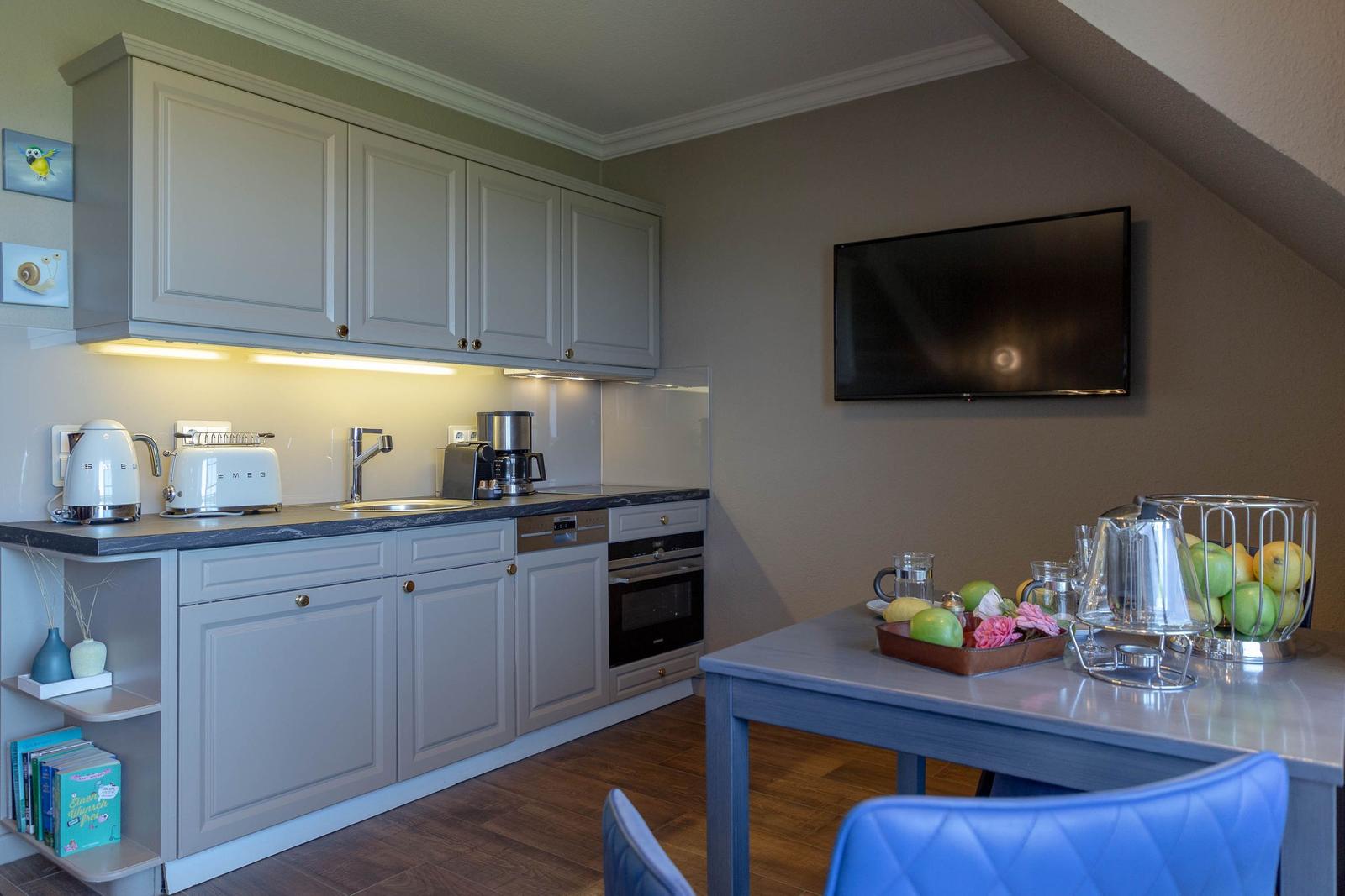 Küche mit Arbeitsplatz, Spüle und integriertem Backofen. An der Wand hängt ein Fernseher.