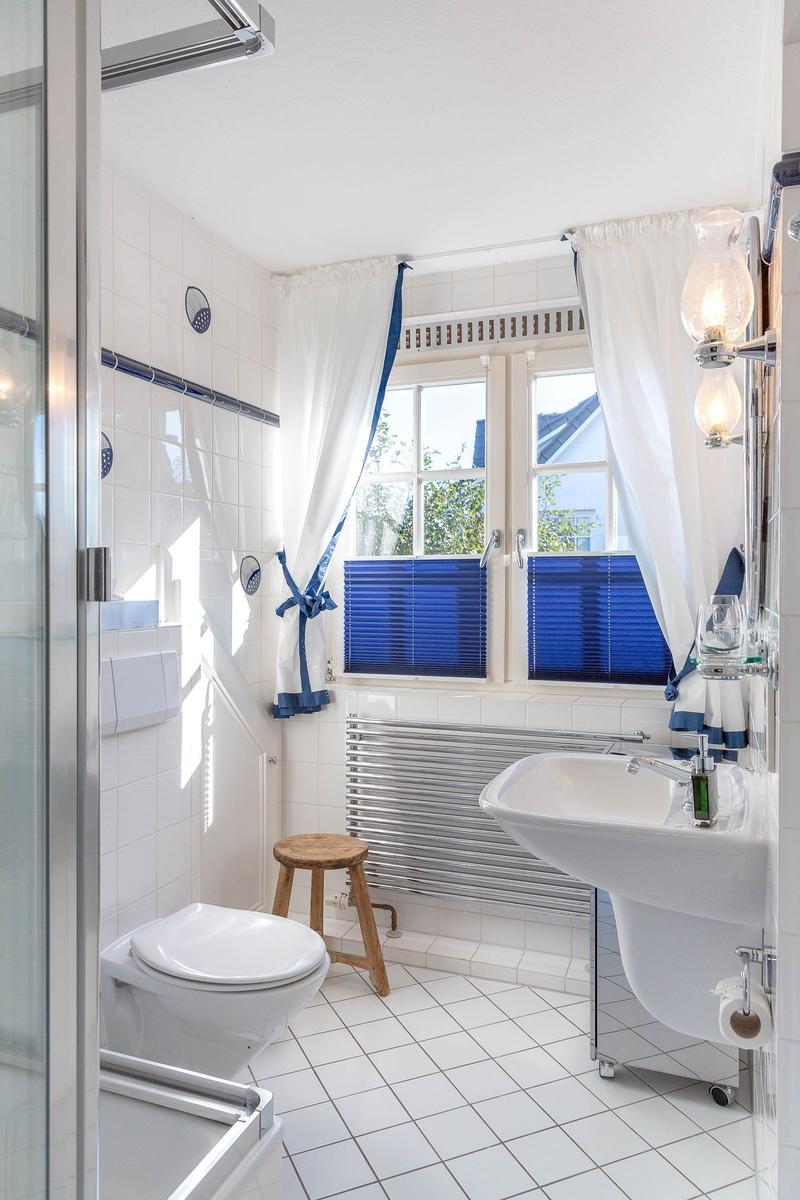 Badezimmer mit Dusche, Toilette, Waschbecken und Fenster mit blauen Jalousien.