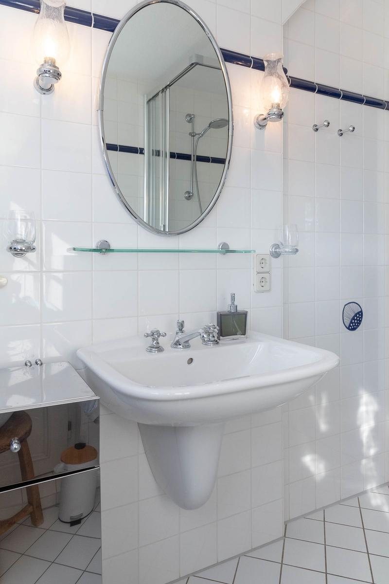 Badezimmer mit Waschbecken, Spiegel und Dusche. Weiße Fliesen und blaue Akzente.