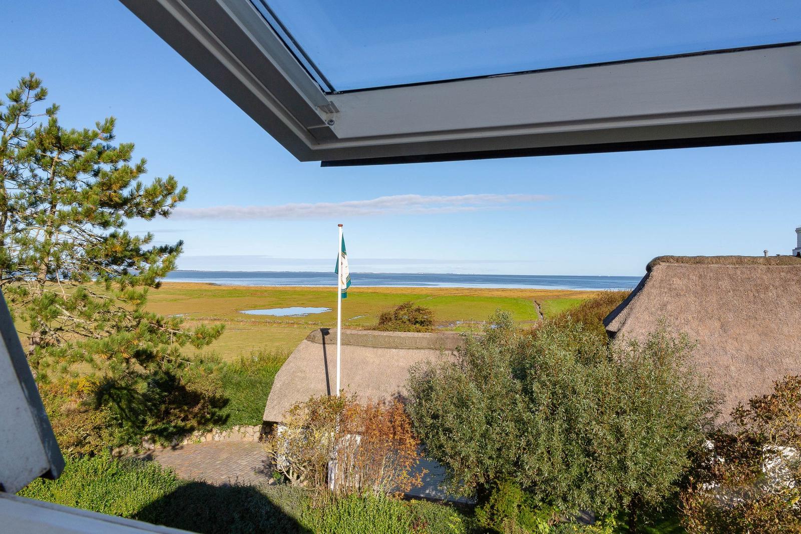 Aus dem Fenster blickt man auf eine grüne Landschaft mit einem See und einem Dach aus Stroh.