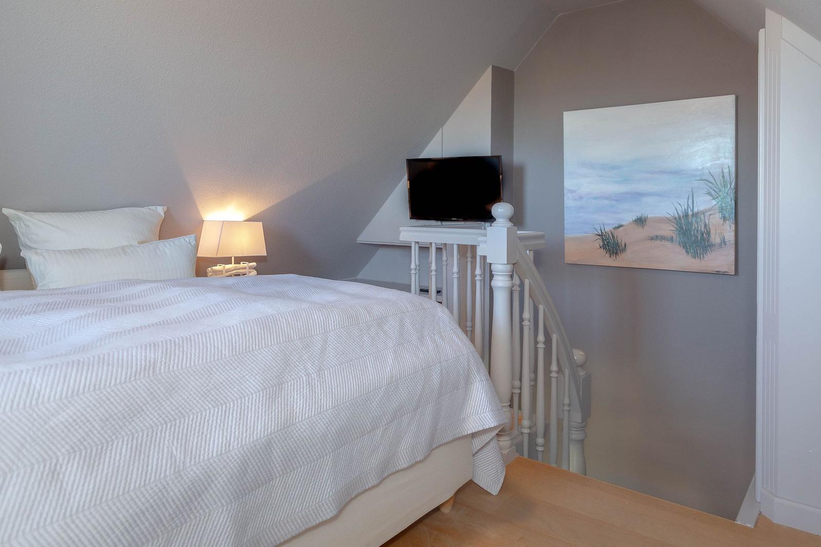 Schlafzimmer mit Bett, Lampe und Fernseher an der Wand.