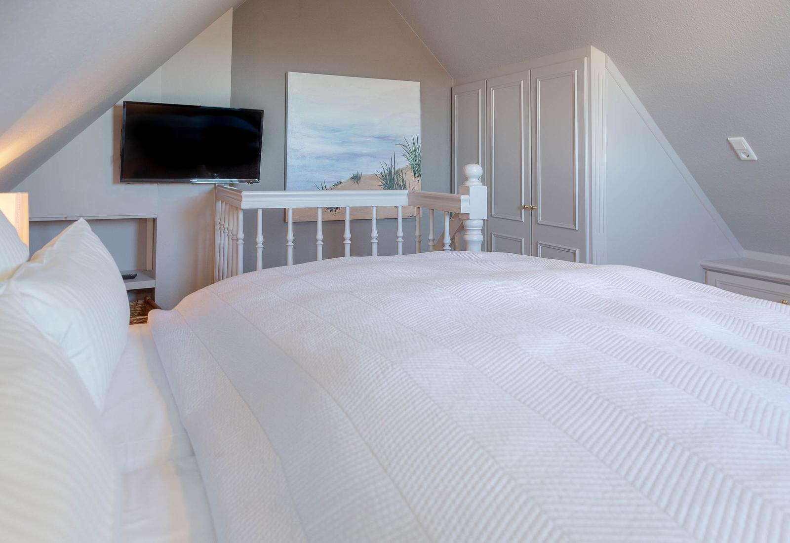 Schlafzimmer mit weißem Bett, Fernseher und Garderobe unter Dachschräge.