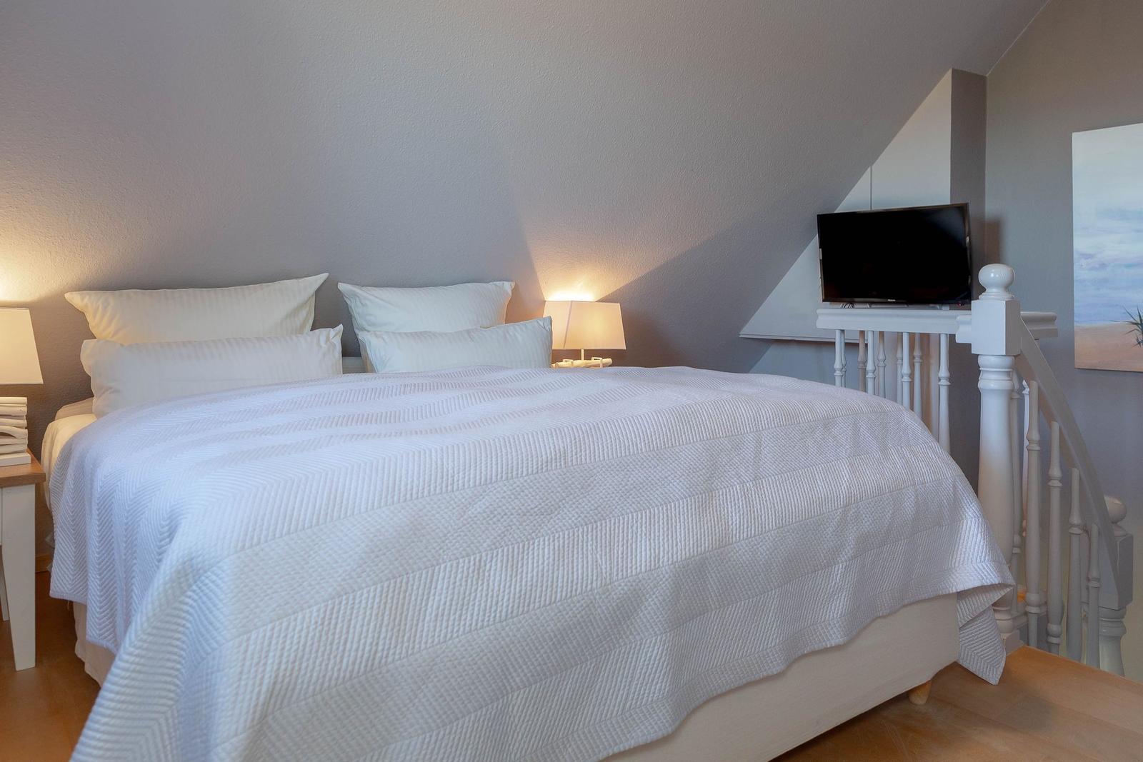 Schlafzimmer mit Bett, Nachttisch, Fernseher und Geländer