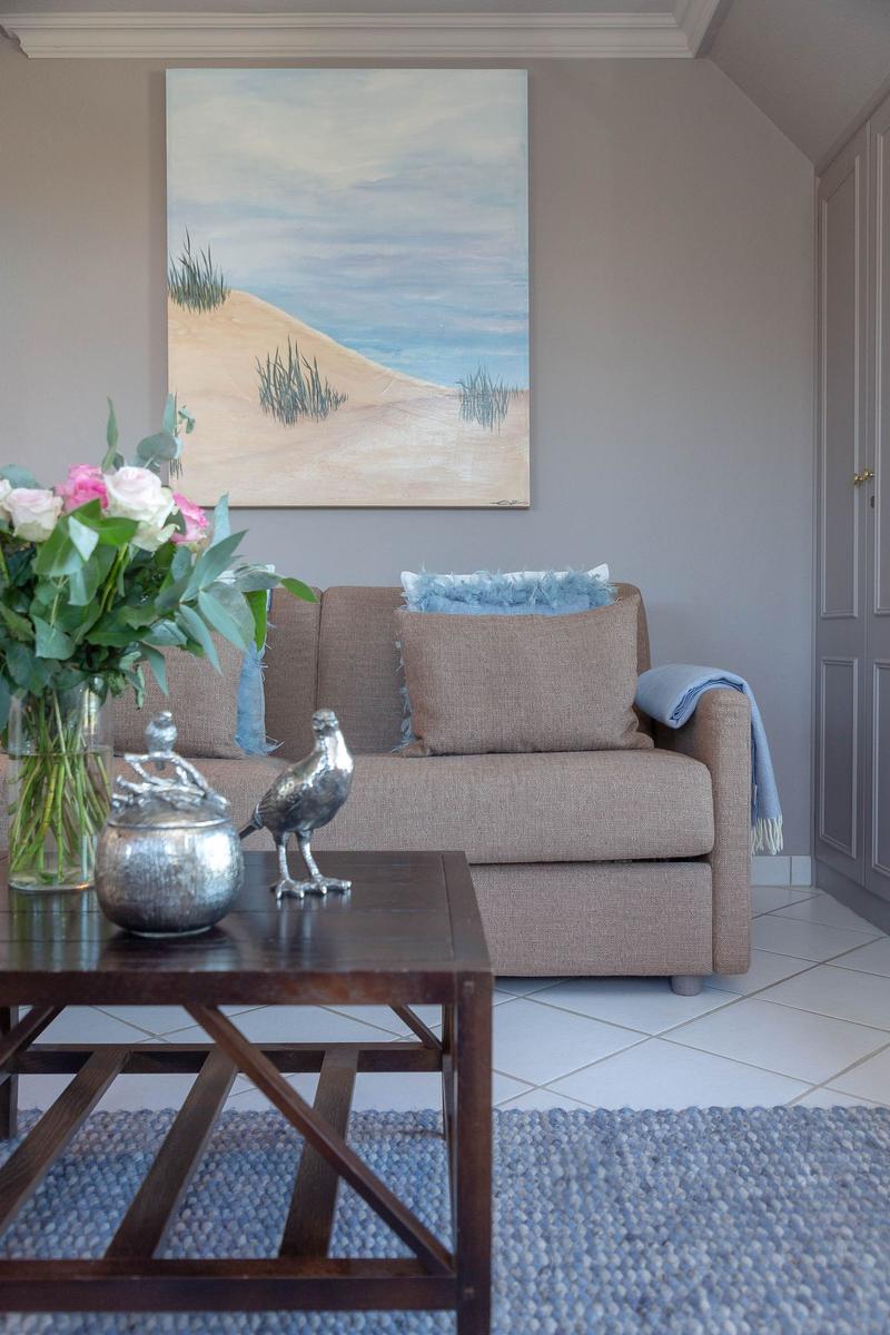 Ein Wohnzimmer mit Sofa, Couchtisch und Wandbild. Blumen und Dekorationen sind vorhanden.