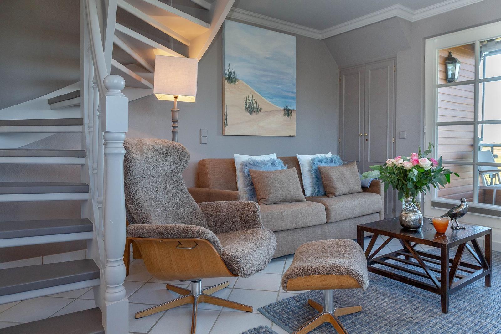 Wohnzimmer mit Sofa, Sessel und Tisch. Hintergrund: Wandgemälde und Treppe.