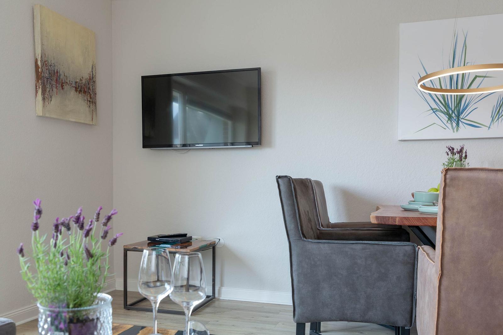 Wohn- und Essbereich mit Fernseher, Tisch und Stühlen sowie Wandbildern.