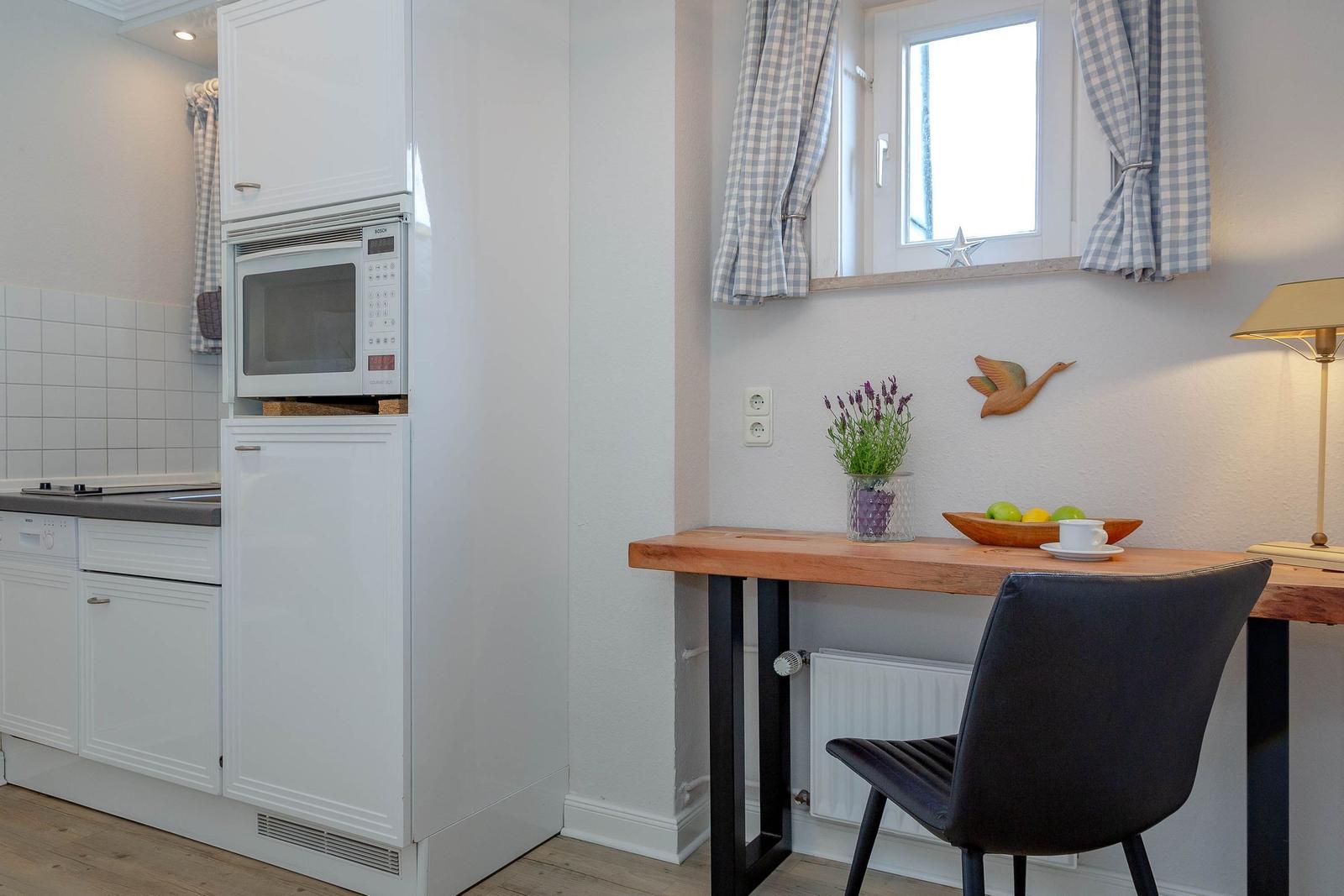 Küche mit Mikrowelle und Arbeitsplatz mit Tisch, Stuhl und Fenster.
