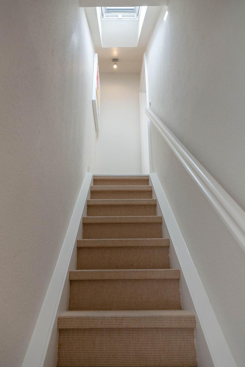 Treppe mit Teppichstufen führt nach oben. Deckenfenster sorgt für Licht.