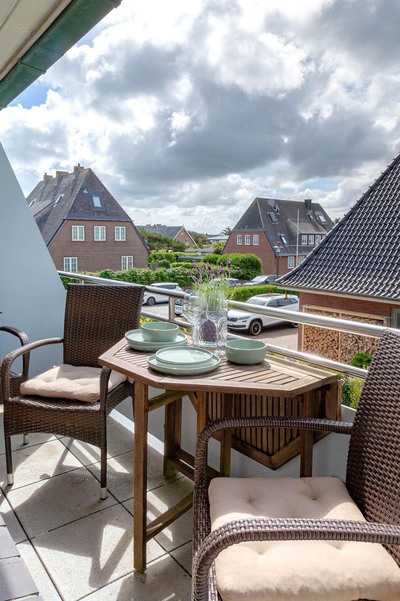 Balkon mit Tisch und zwei Stühlen, Blick auf Wohnhäuser und Straße.