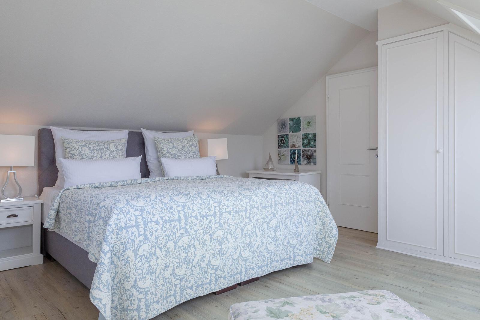 Schlafzimmer mit Doppelbett, weißen Nachttischen und Kleiderschrank unter schrägem Dach.