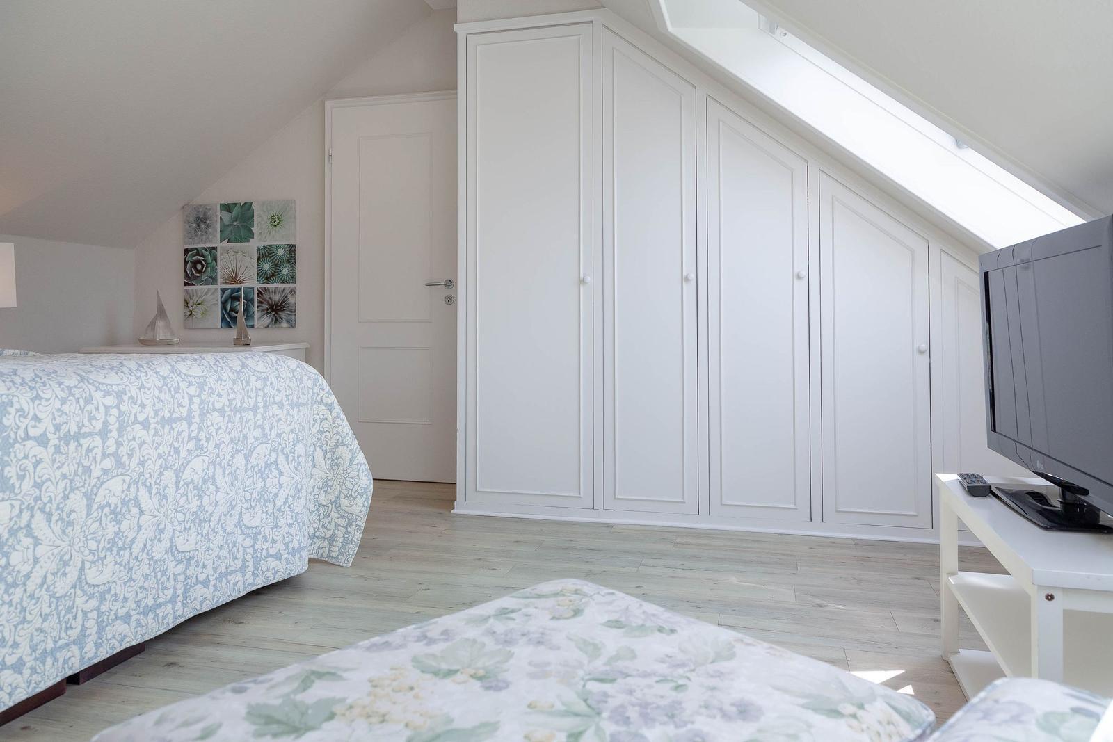 Schlafzimmer mit Dachschrägen, weißem Schrank und Bett mit Muster