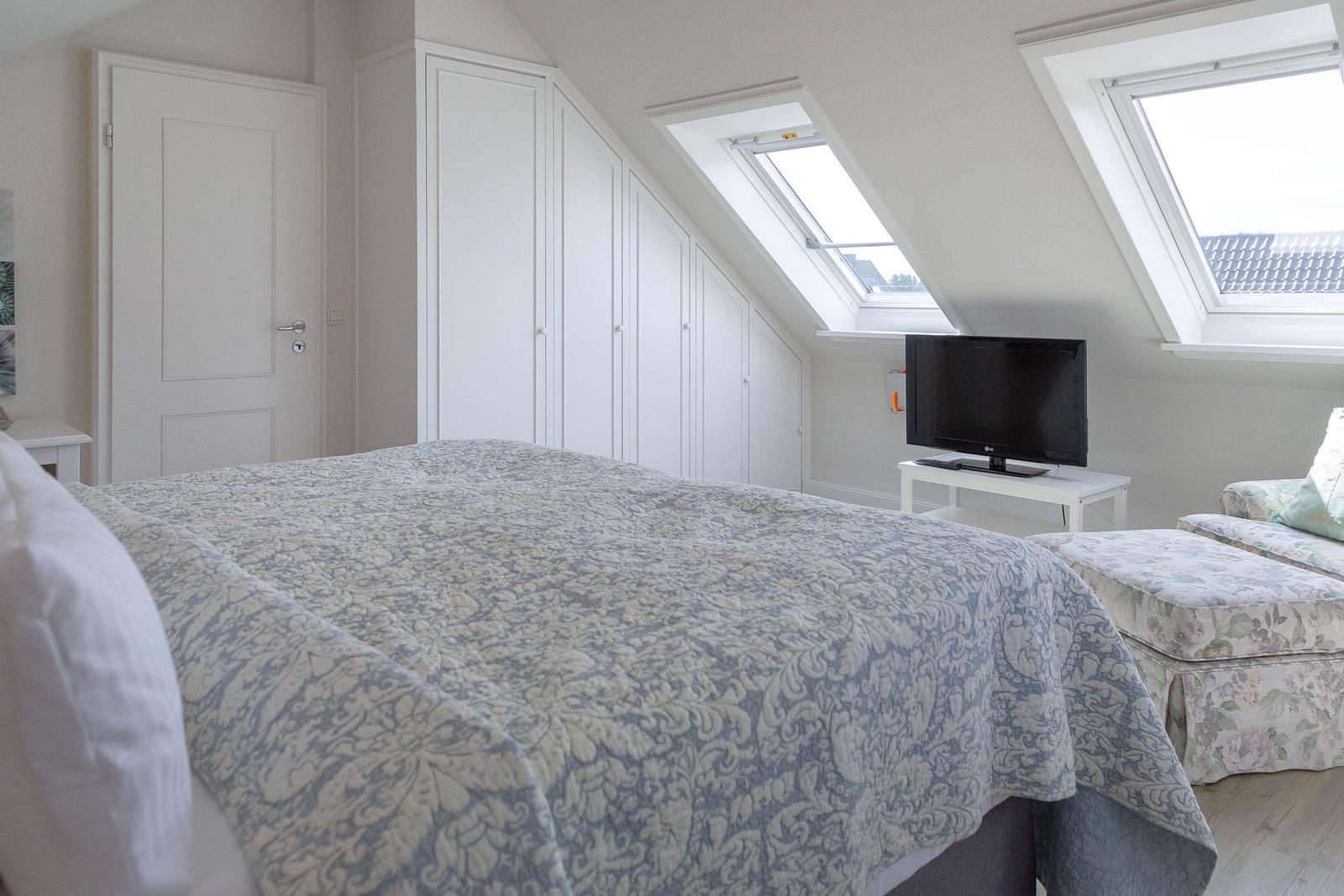 Schlafzimmer mit Dachschrägen, zwei Dachfenstern, Bett, Kleiderschrank und Fernseher.