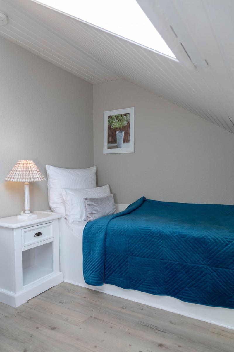 Schlafzimmer mit Dachschräge, blauer Bettdecke und Nachttisch mit Lampe.