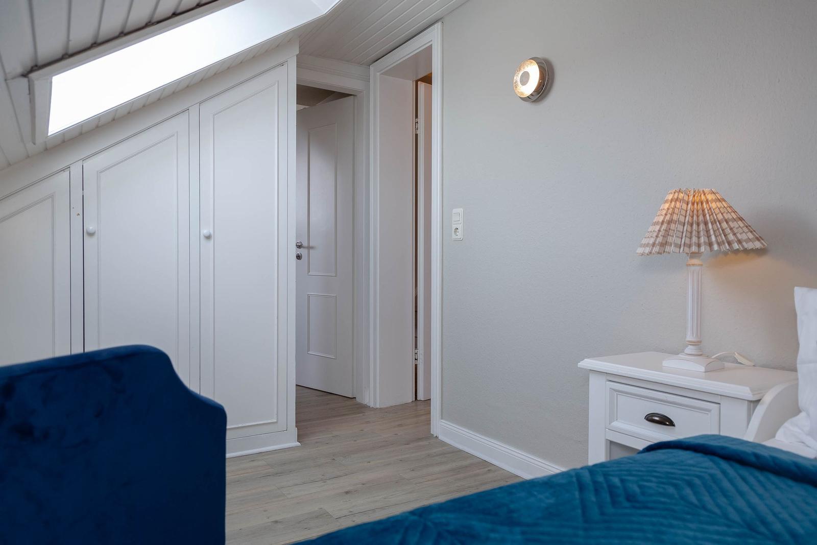 Schlafzimmer mit blauem Bett, weißem Schrank und Nachttisch mit Lampe.