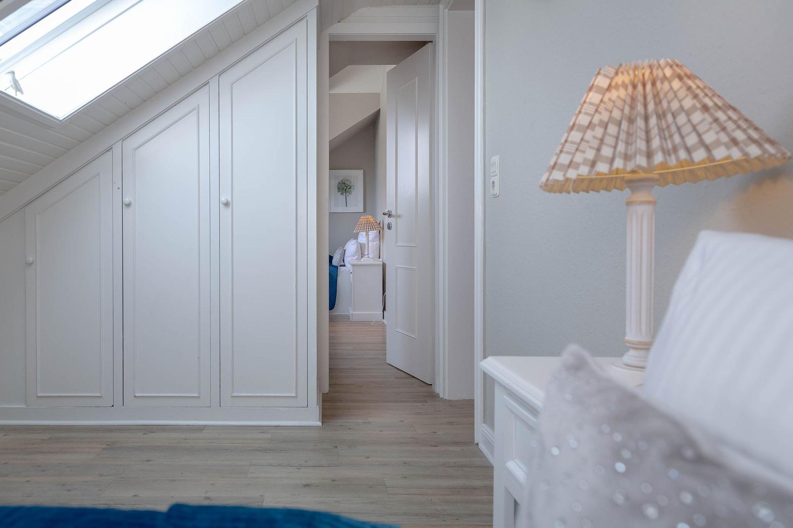 Schlafzimmer mit Dachschrägen, weißen Schränken und Holzboden. Lampe auf Nachttisch.