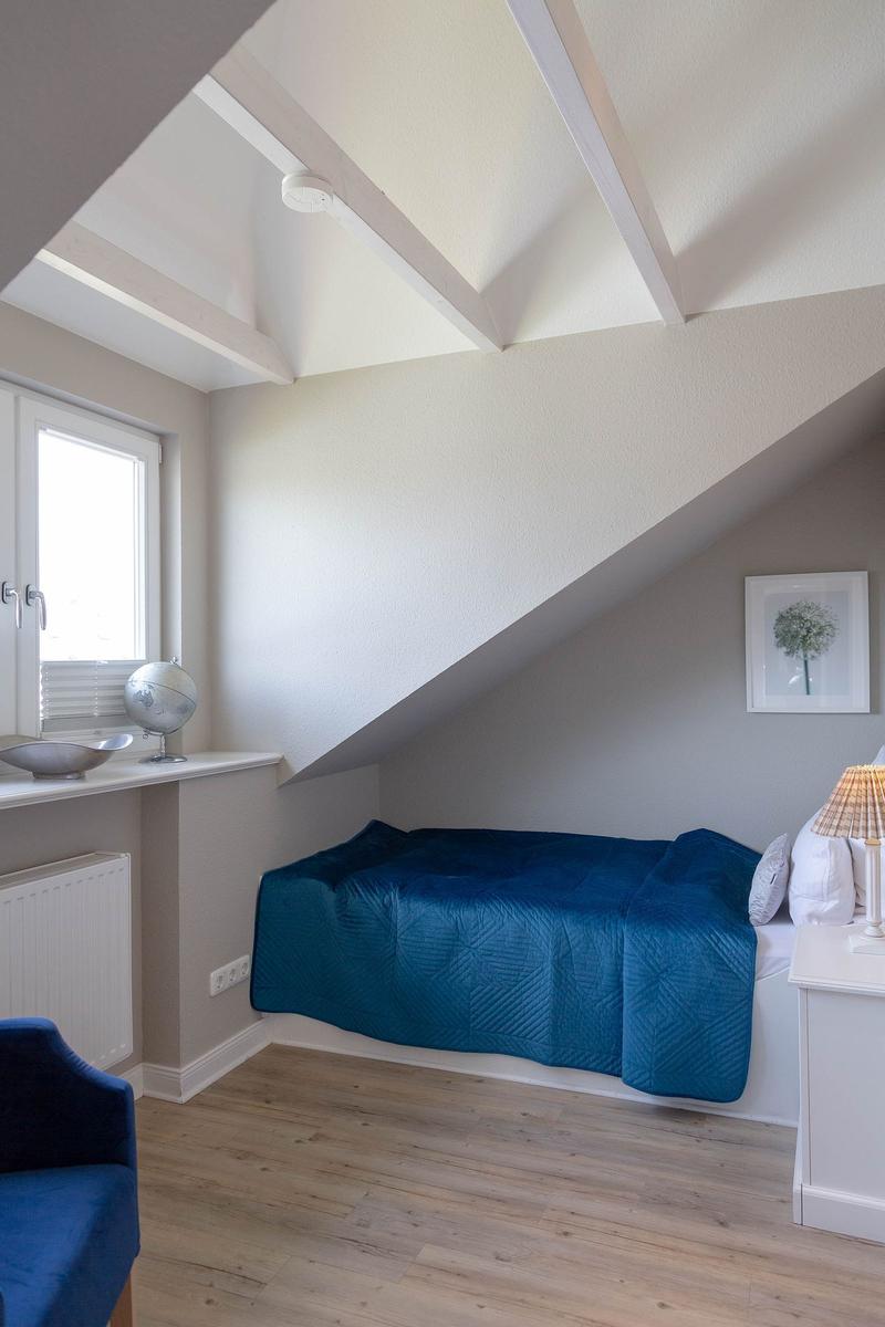Ein Schlafzimmer mit Dachschrägen, blauer Bettwäsche und Holzboden.