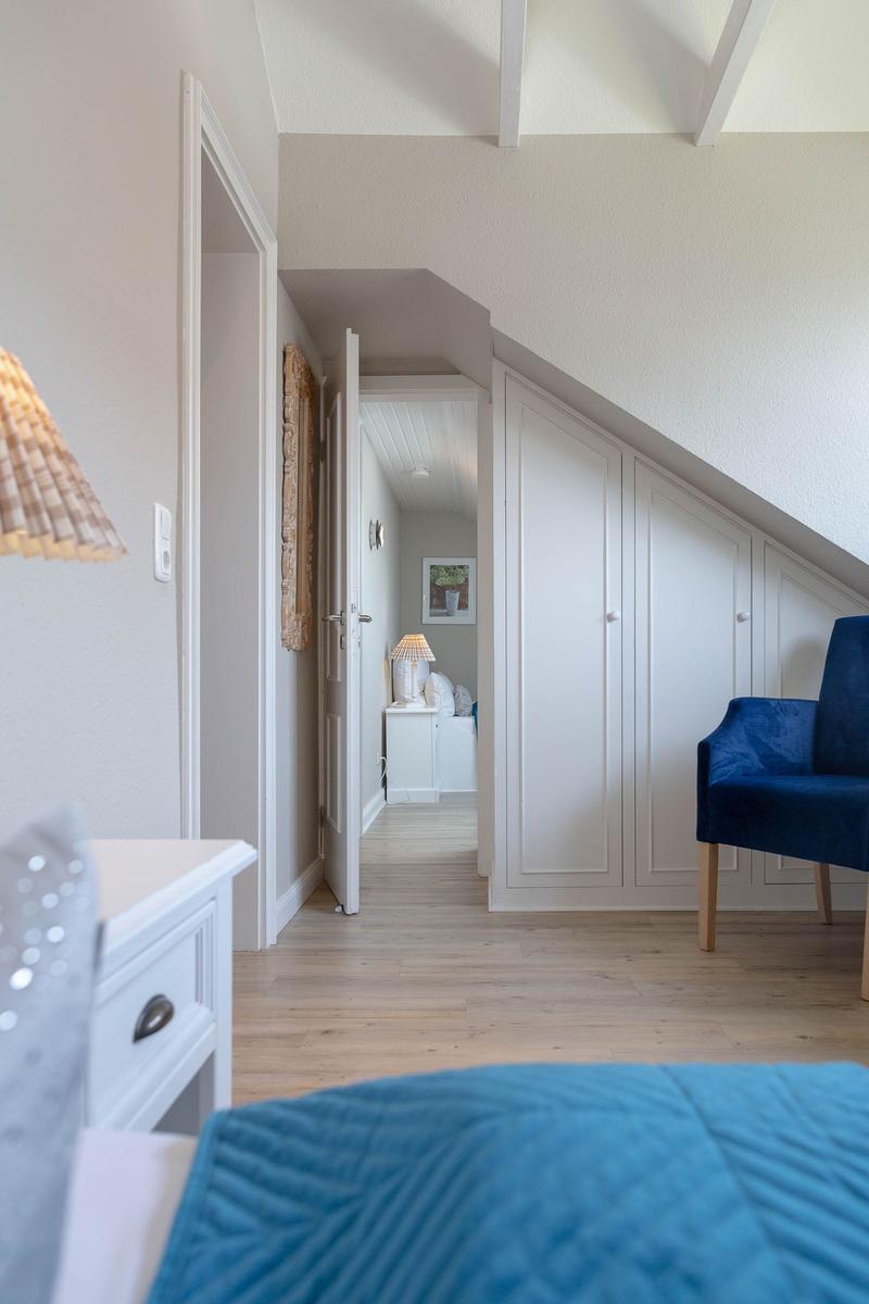 Schlafzimmer mit blauer Sitzgelegenheit und weißen Schränken unter Dachschrägen.