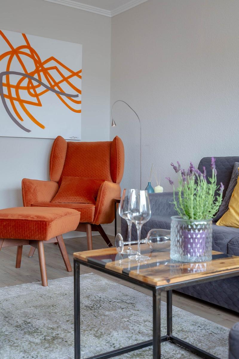 Ein Wohnzimmer mit orangefarbenem Sessel, grauem Sofa und Holztisch.