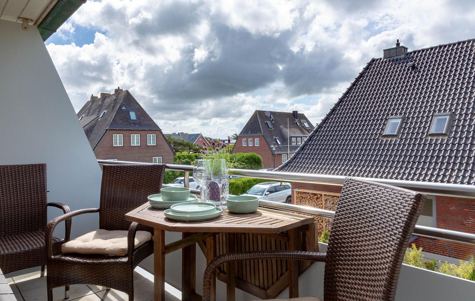 Terrasse mit Tisch und Stühlen, Blick auf Dächer und Himmel.