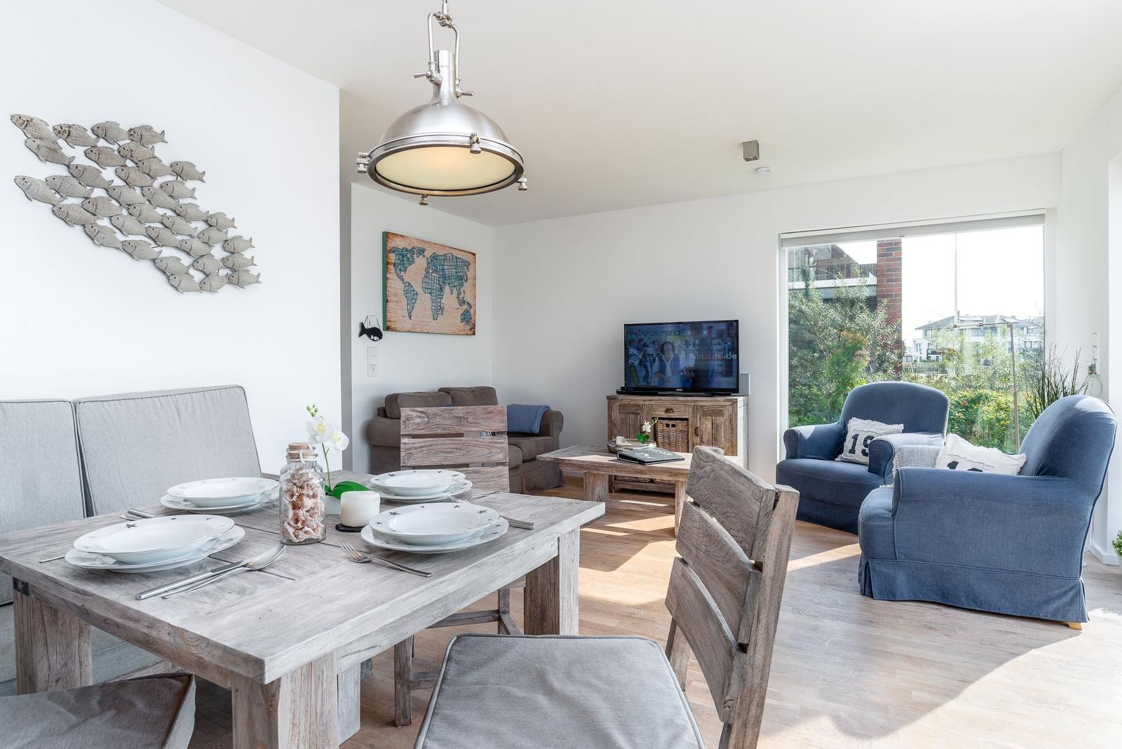 Essbereich mit Tisch und Stühlen, Wohnbereich mit Sofa und Fernseher, große Fenster mit Blick auf Garten.