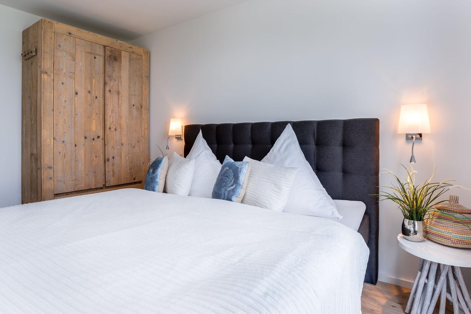 Schlafzimmer mit Bett, Holzschrank und Nachttisch mit Pflanze.