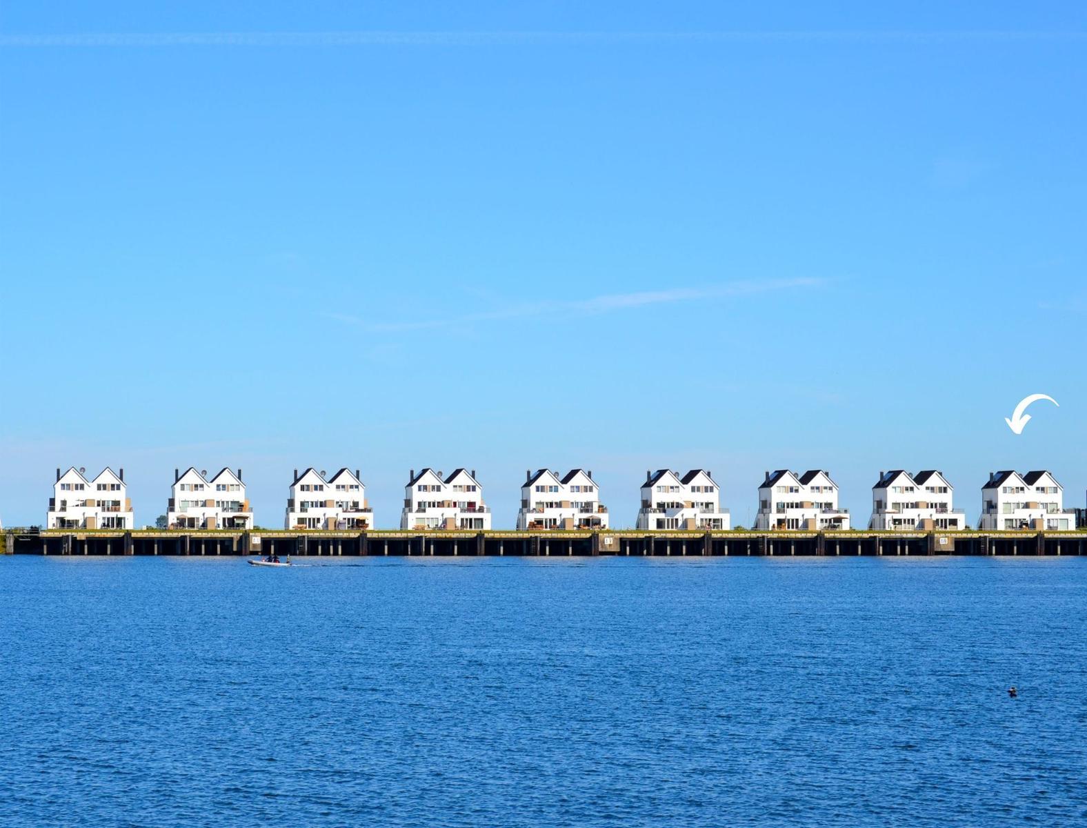 Reihe weißer Häuser am Wasser unter blauem Himmel mit Boot im Vordergrund.