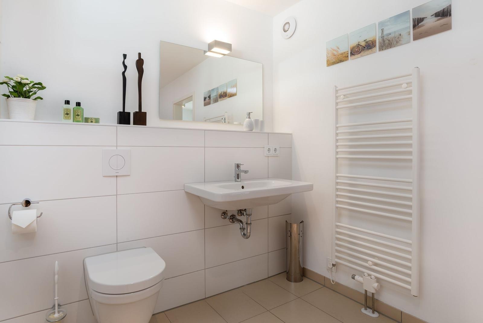 Badezimmer mit Toilette, Waschbecken und Heizkörper. Wandbilder und Pflanze sichtbar.