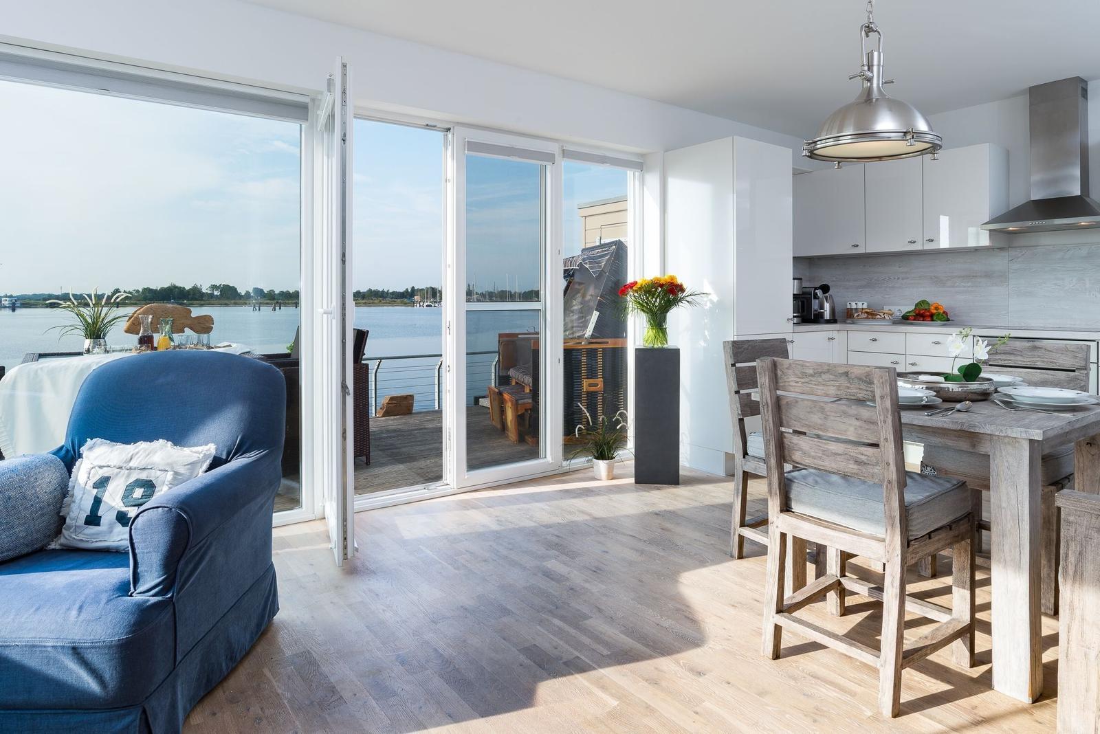 Wohnküche mit Blick auf Wasser, blauer Sessel und Holztisch mit Stühlen.