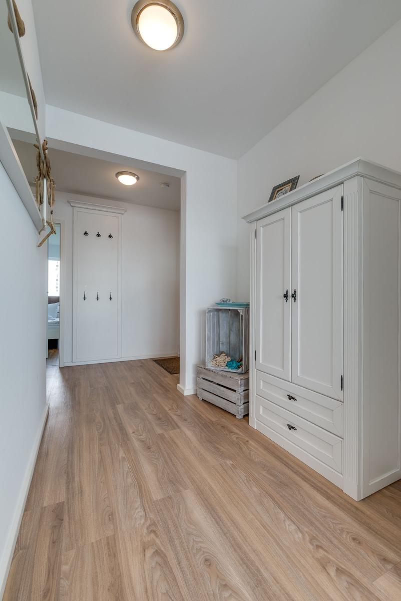 Hallway with wooden floor, white wardrobe, and coat hooks on the wall.