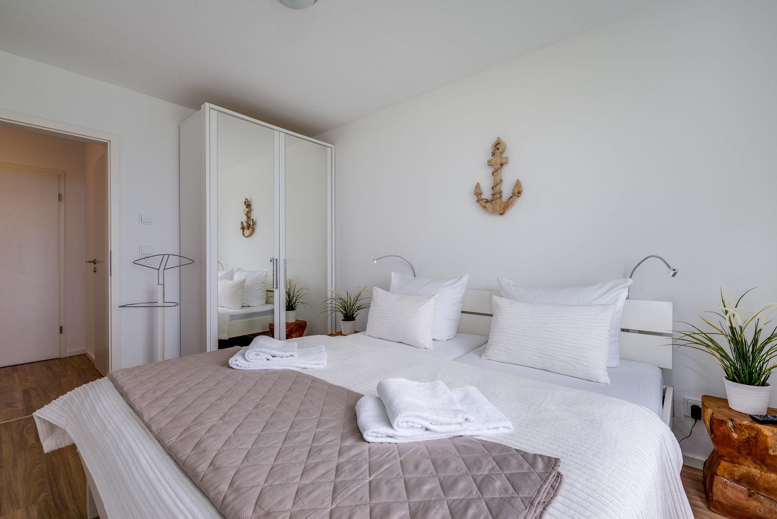Bedroom with double bed, mirrored wardrobe, and standing lamp. Wall decor with anchor.