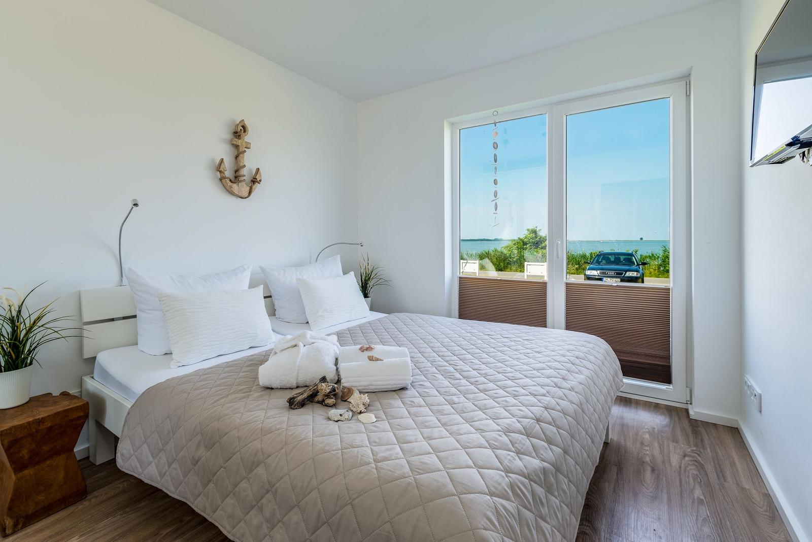 Bedroom with water view, bed with white pillows and wooden floor.