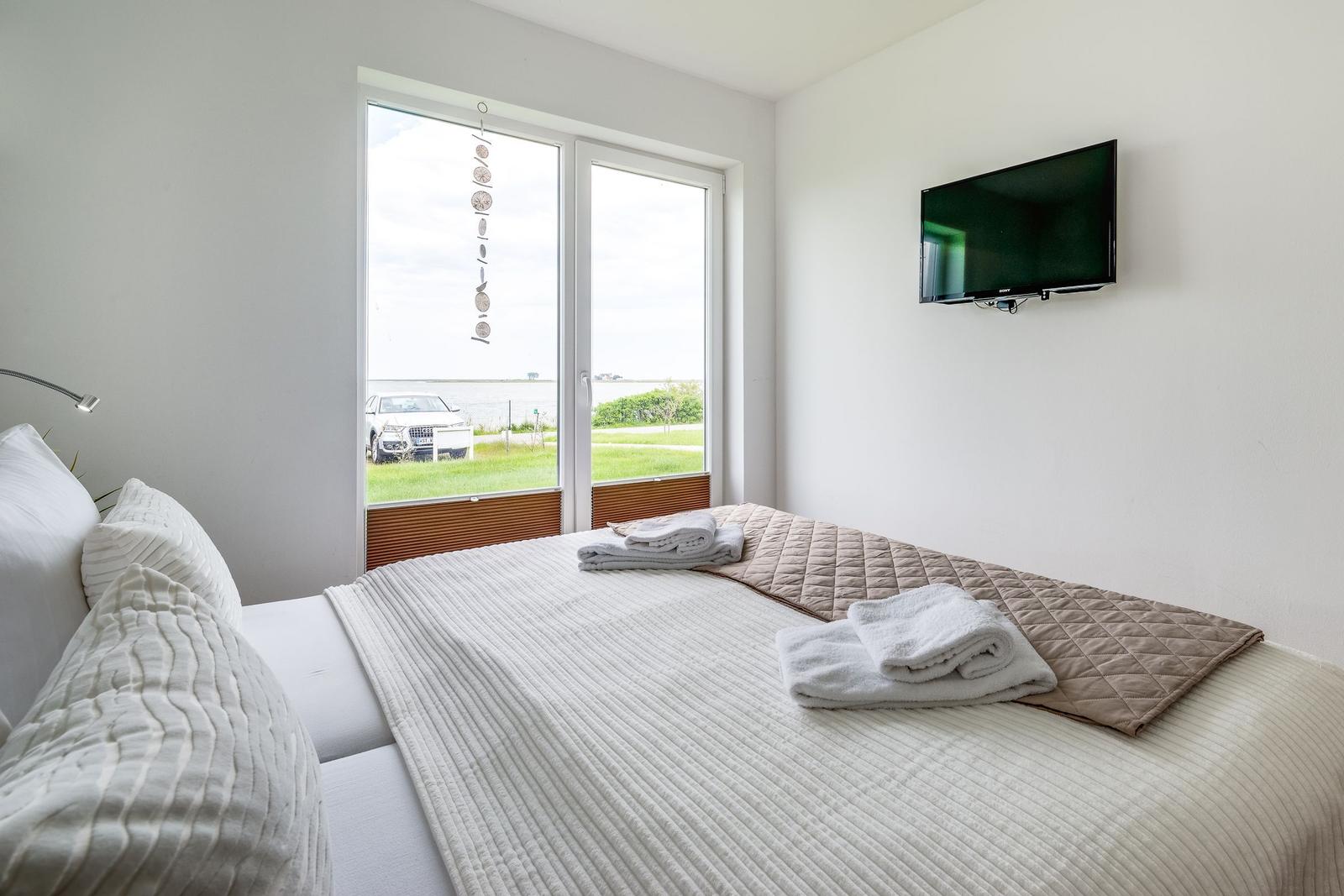 Bedroom with bed, TV, and view of green area and water.