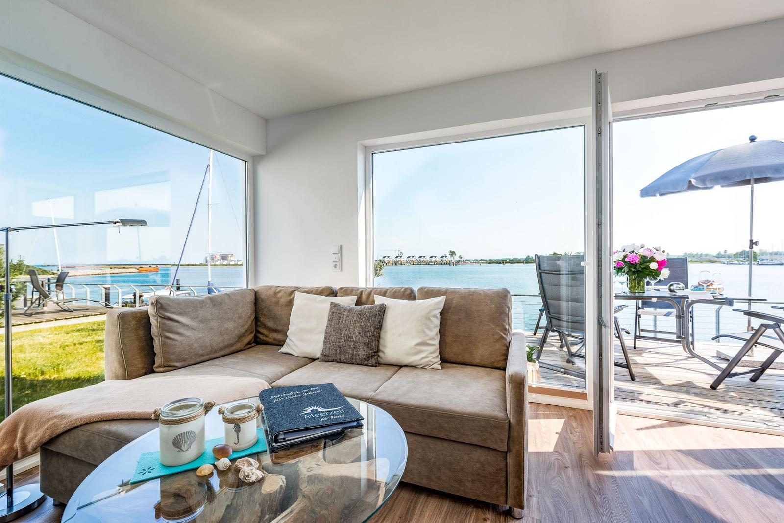 Living area with sofa, glass table, and view of water and terrace.