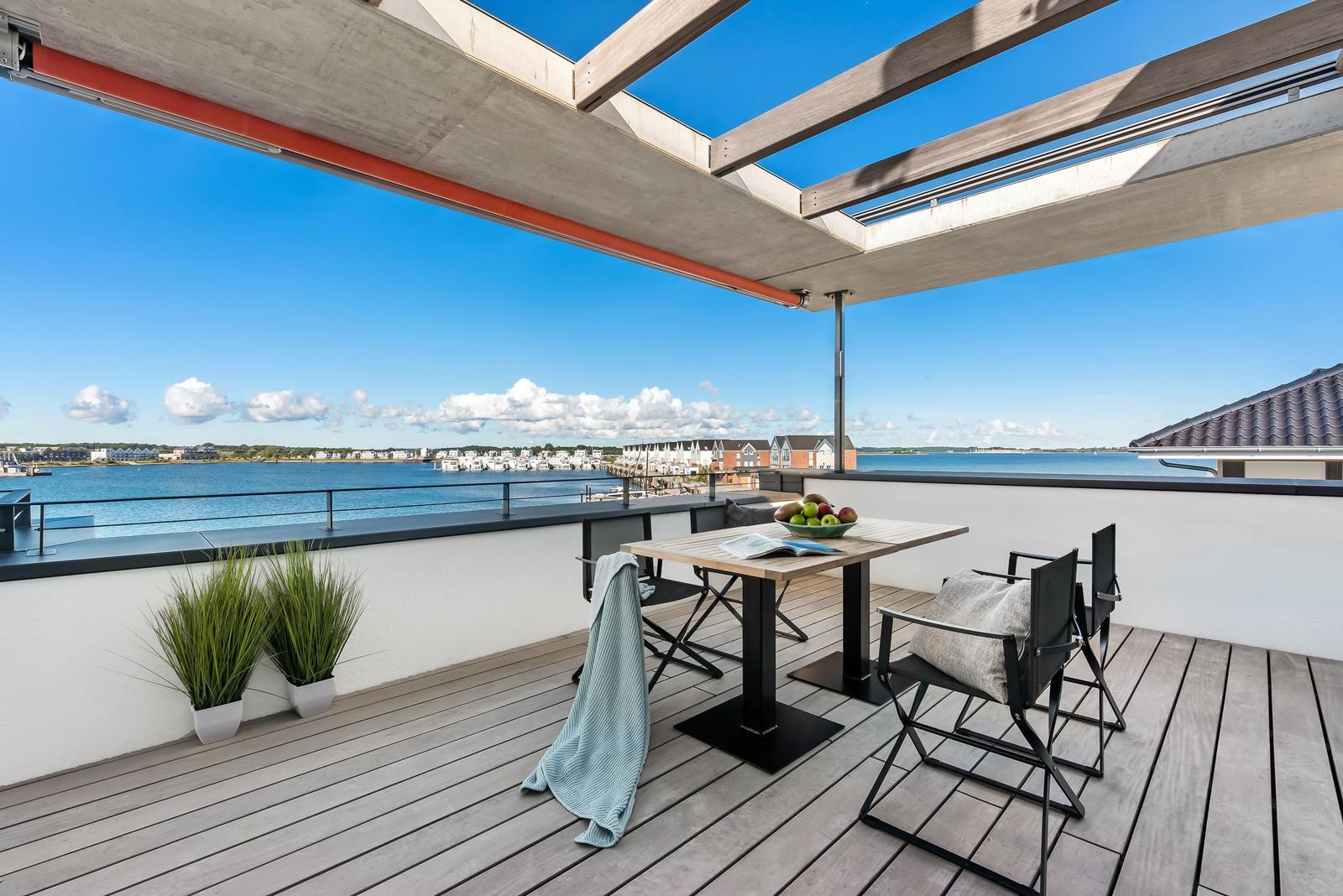 Terrasse mit Tisch, Stühlen und Blick auf Wasser und Häuser.