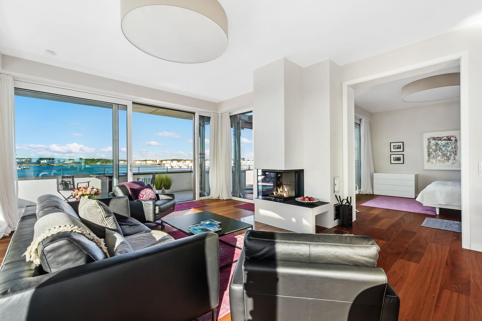 Wohnung mit Blick auf Wasser, Kamin und Schlafzimmer im Hintergrund.
