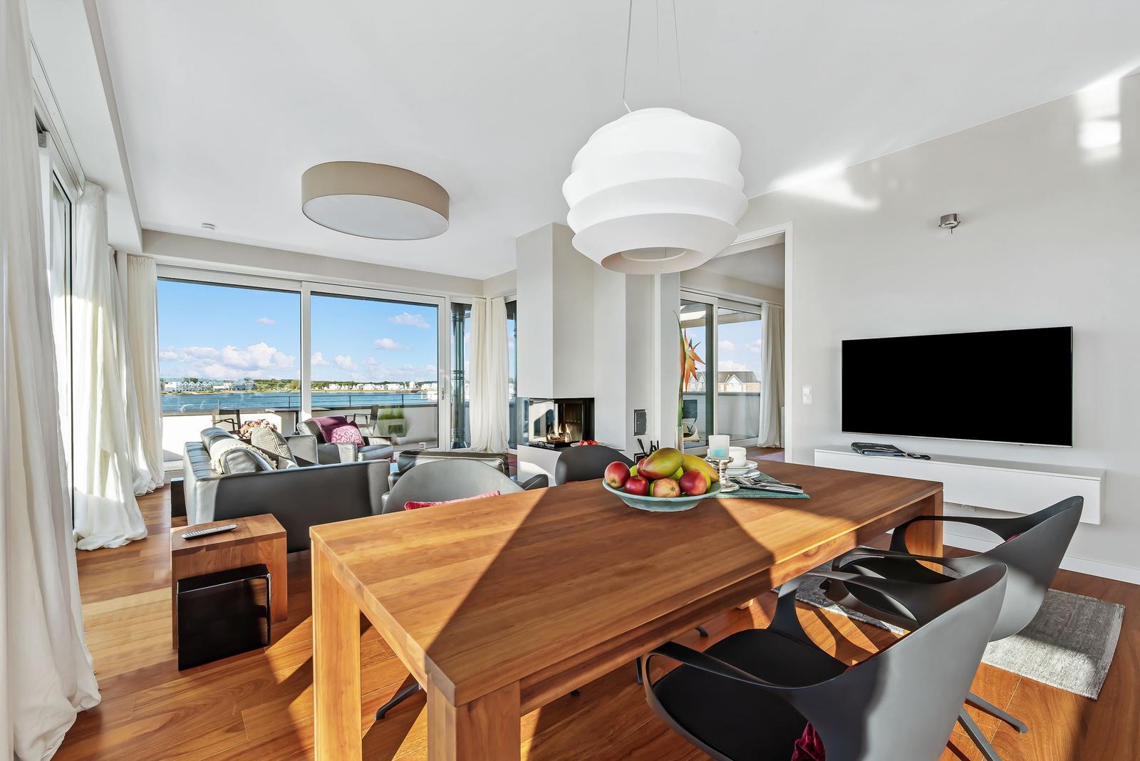 Modernes Wohn- und Esszimmer mit Blick auf Wasser. Esstisch mit Stühlen und Fernseher.