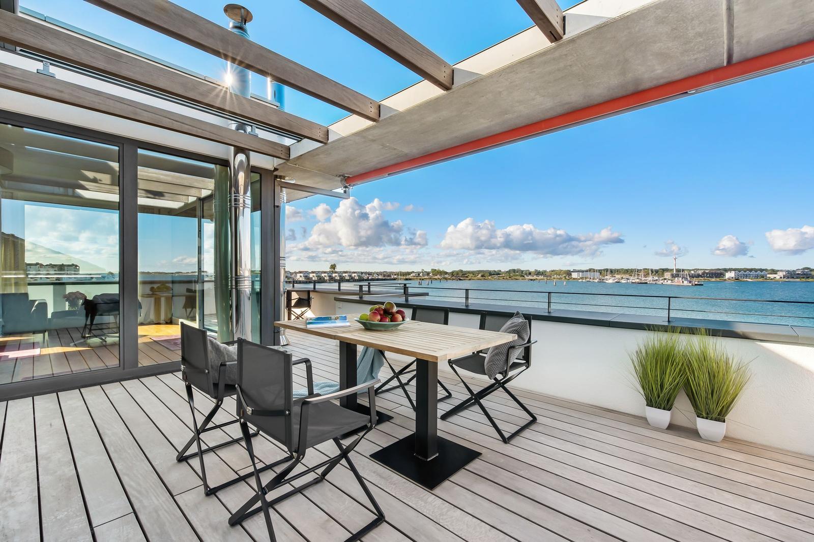 Terrasse mit Tisch, Stühlen und Meerblick. Holzdielen und Pflanzen.