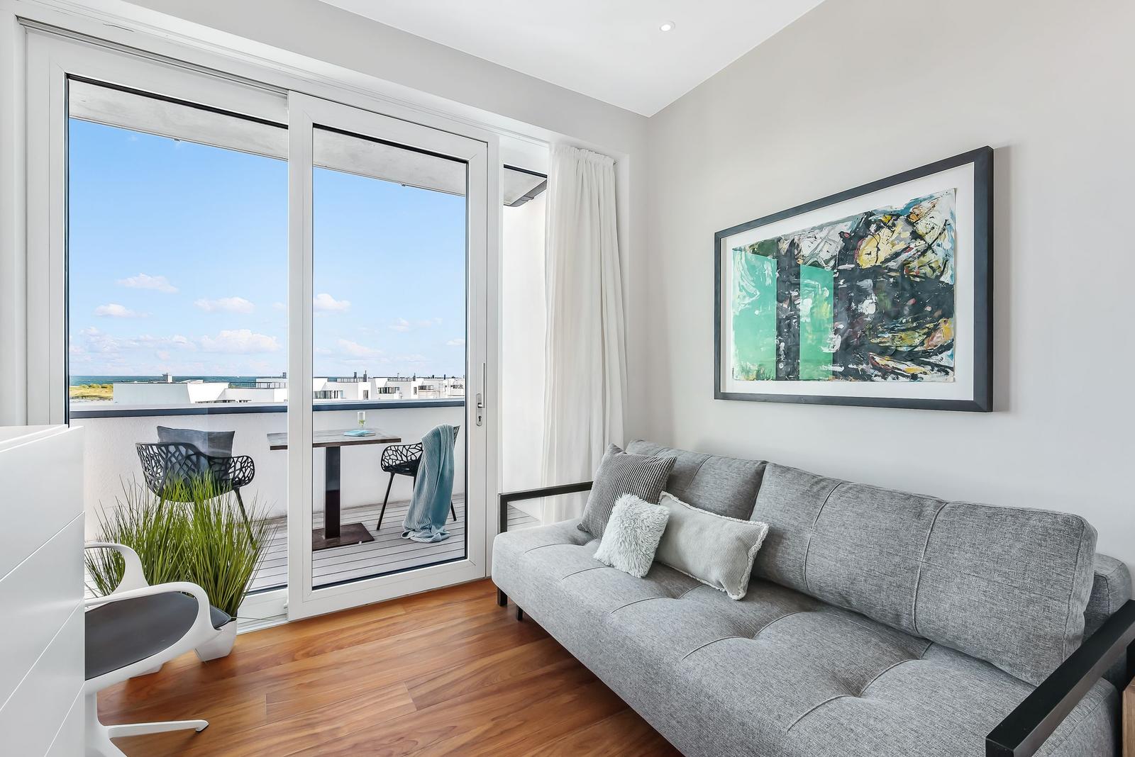 Ein Wohnzimmer mit grauem Sofa, Holzboden und Balkon mit Tisch und Stühlen.