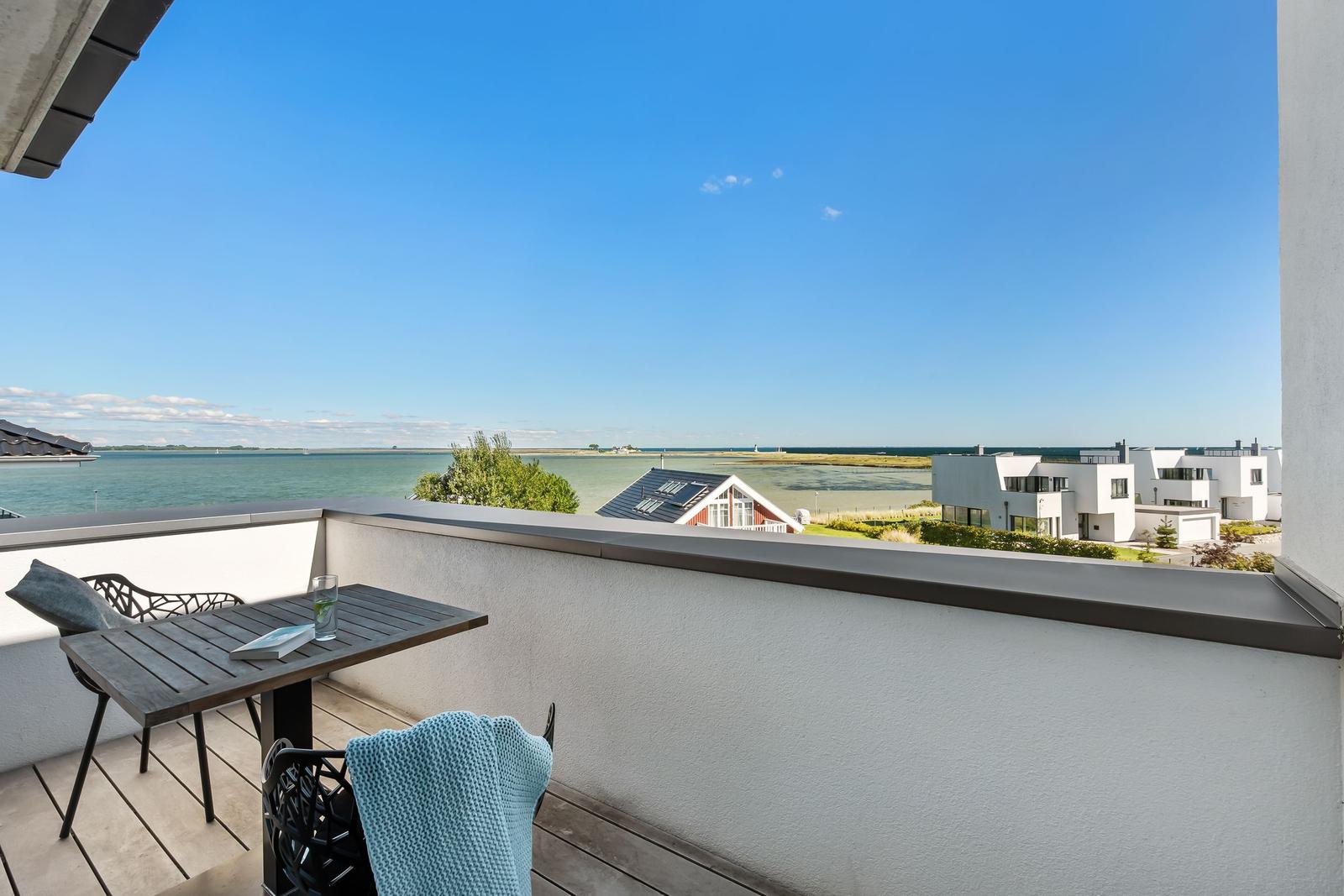 Terrasse mit Tisch und Stühlen, Blick auf Wasser und moderne Gebäude.