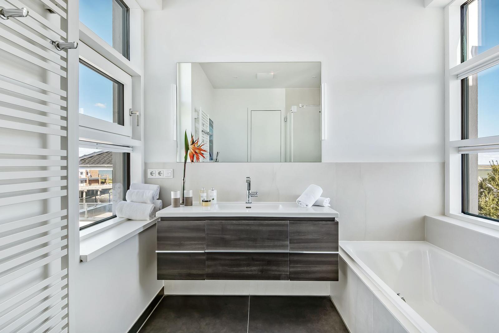 Badezimmer mit Waschtisch, Badewanne und Fenstern.