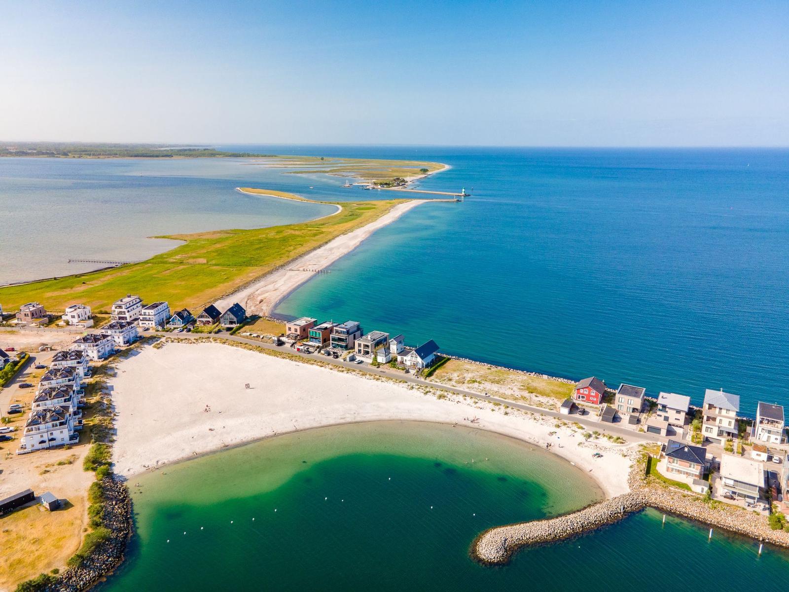 Aerial view of a coastal village with beach, houses, and clear blue waters.