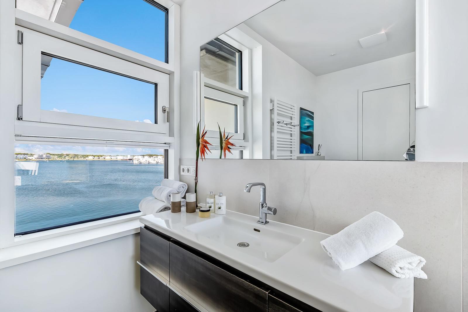 Badezimmer mit Blick auf Wasser und Himmel durch großes Fenster.