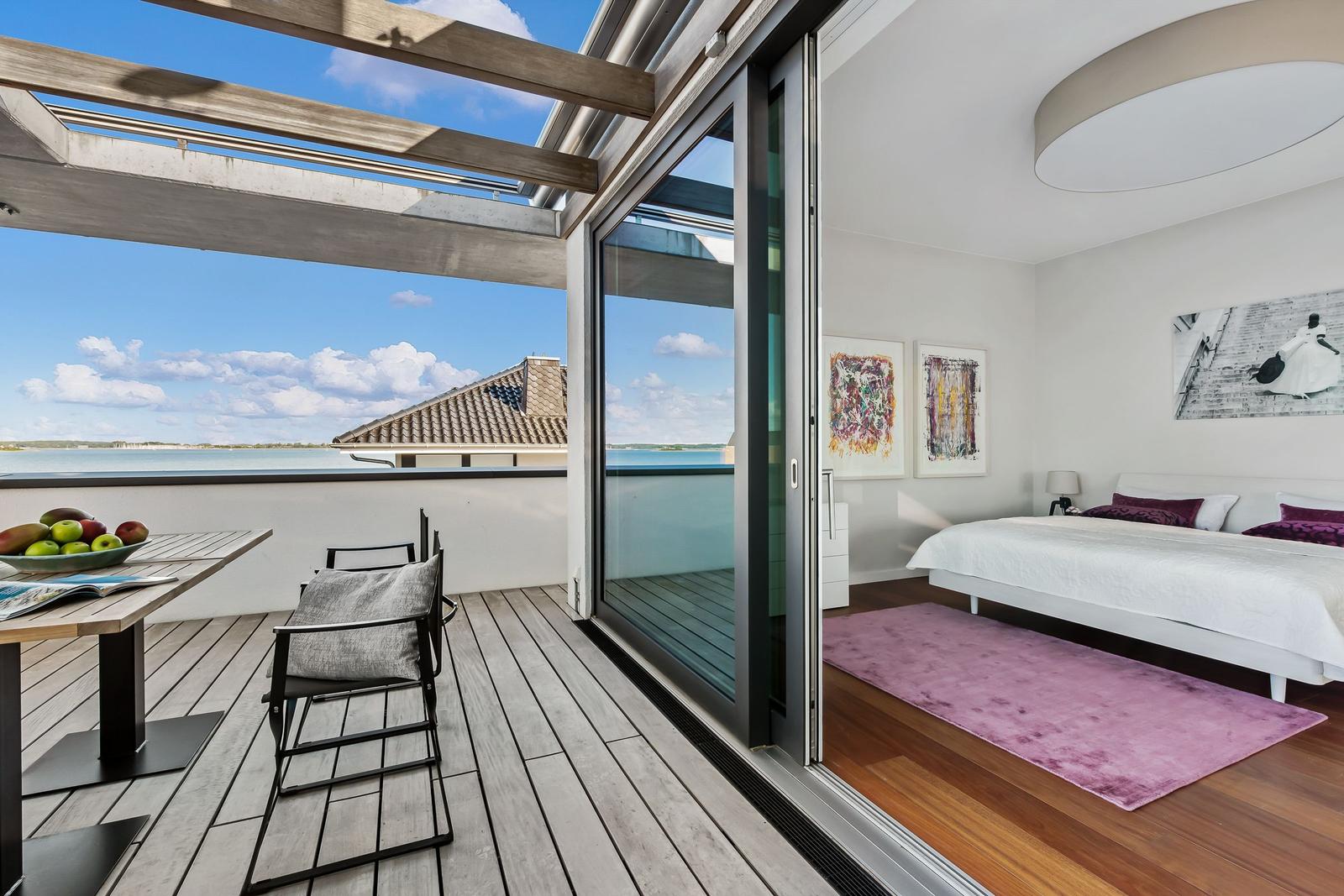 Schlafzimmer mit Blick auf Terrasse und Wasser. Holzboden, Bett, Kunst an der Wand.